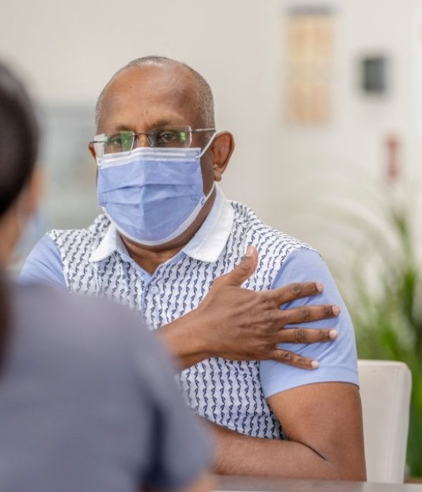 65 year old Trinidadian man meeting with a female medical professional in the health clinic. Both are wearing masks to prevent the transfer of germs.